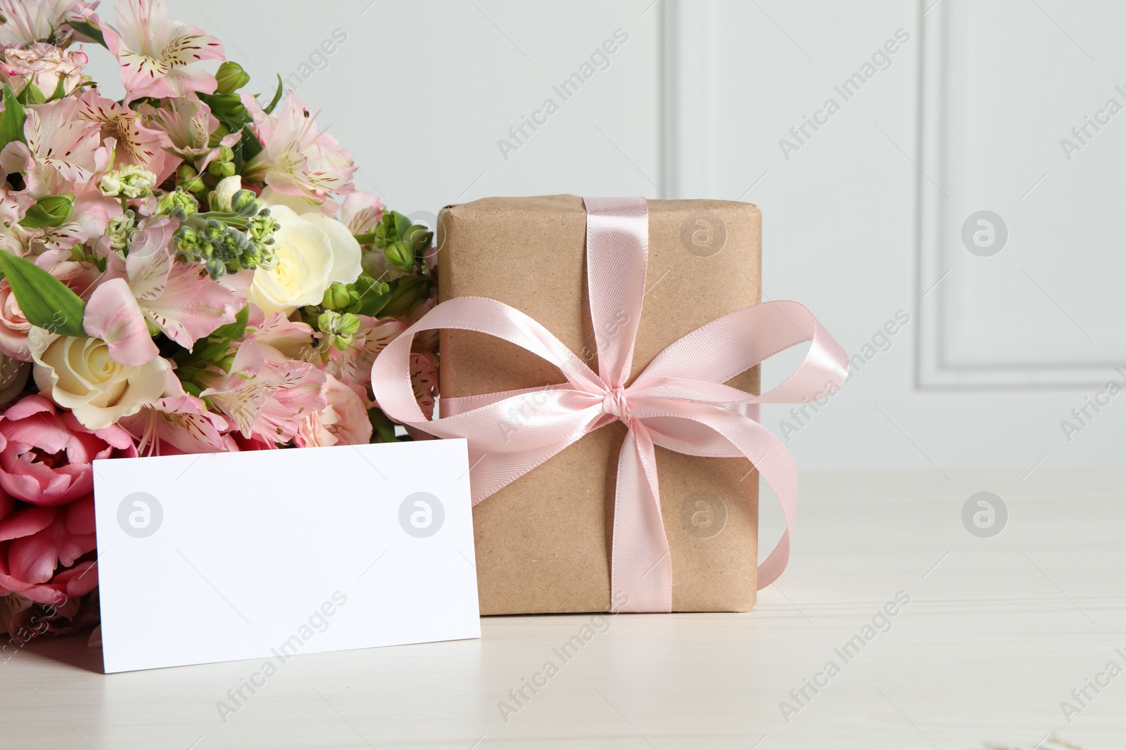 Photo of Happy Mother's Day. Gift box, blank card and bouquet of beautiful flowers on white table. Space for text