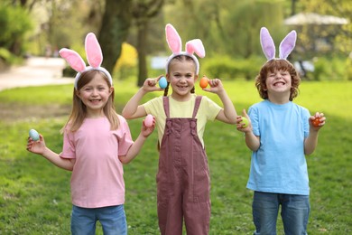 Photo of Easter celebration. Cute little children in bunny ears holding painted eggs outdoors