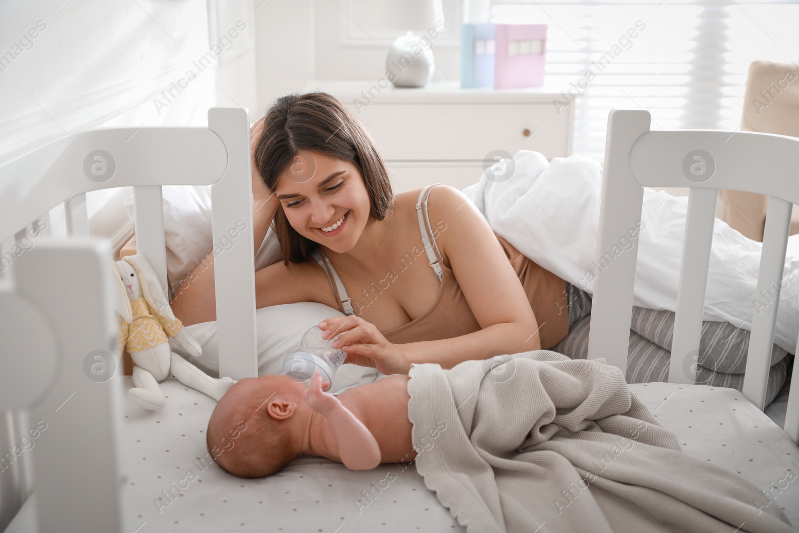 Photo of Happy young mother feeding her newborn baby from bottle at home