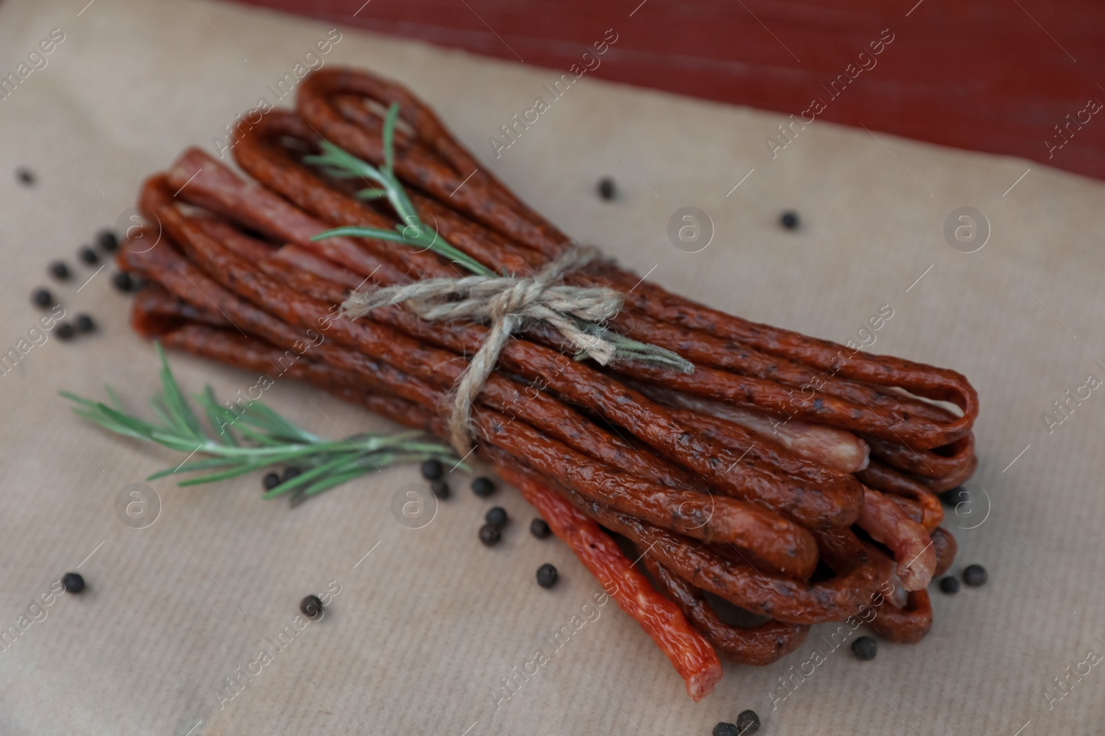 Photo of Tasty dry cured sausages (kabanosy) and spices on parchment paper, closeup