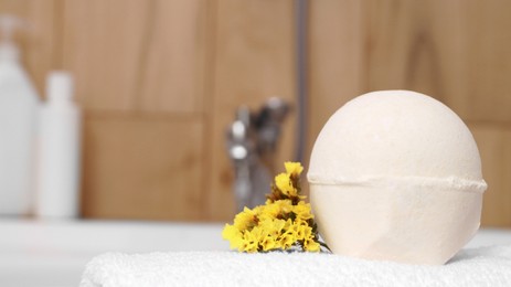 Photo of Towel with bath bomb and flowers on tub indoors, closeup. Space for text