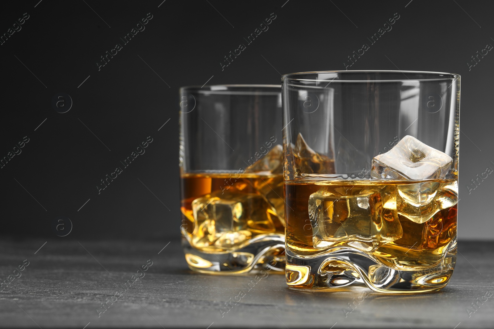 Photo of Whiskey and ice cubes in glasses on grey table, closeup. Space for text