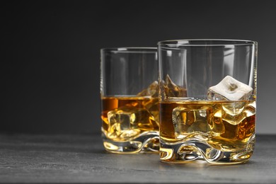 Photo of Whiskey and ice cubes in glasses on grey table, closeup. Space for text