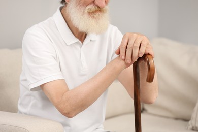 Photo of Senior man with walking cane on sofa indoors, closeup