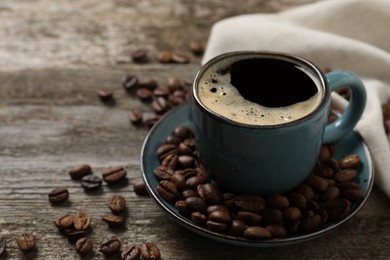 Photo of Cup of aromatic coffee and beans on wooden table, closeup. Space for text