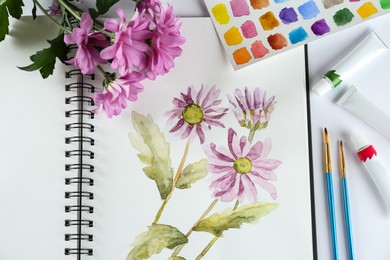 Photo of Painting of chrysanthemums in sketchbook, flowers and supplies on white background, flat lay