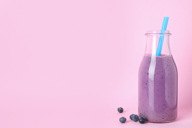 Tasty milk shake in bottle and blueberries on pink background. Space for text