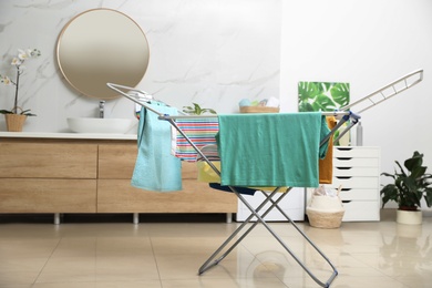 Photo of Clean laundry hanging on drying rack in bathroom