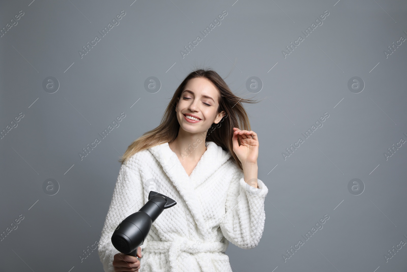 Photo of Beautiful young woman using hair dryer on grey background