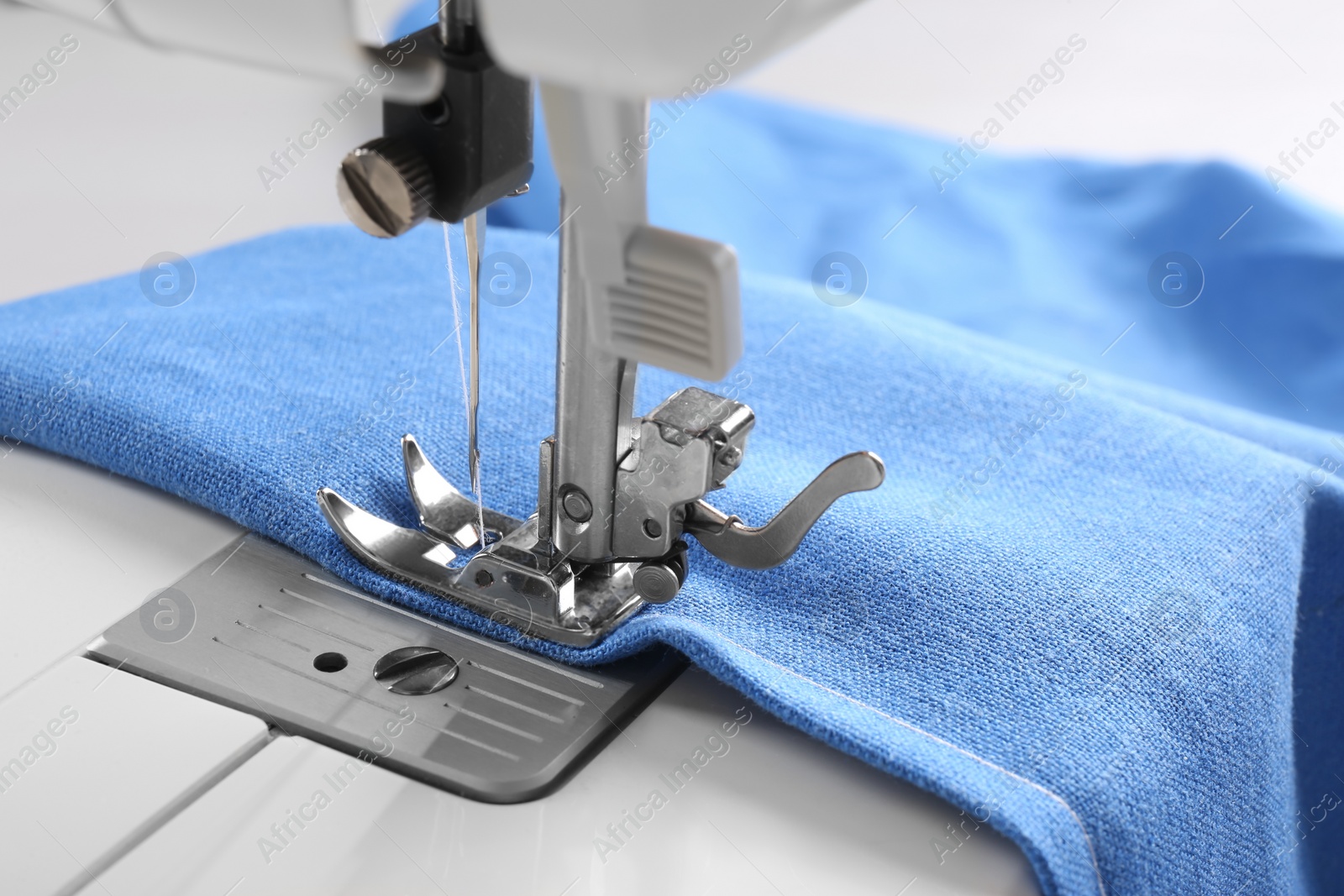 Photo of Modern sewing machine with blue cloth, closeup