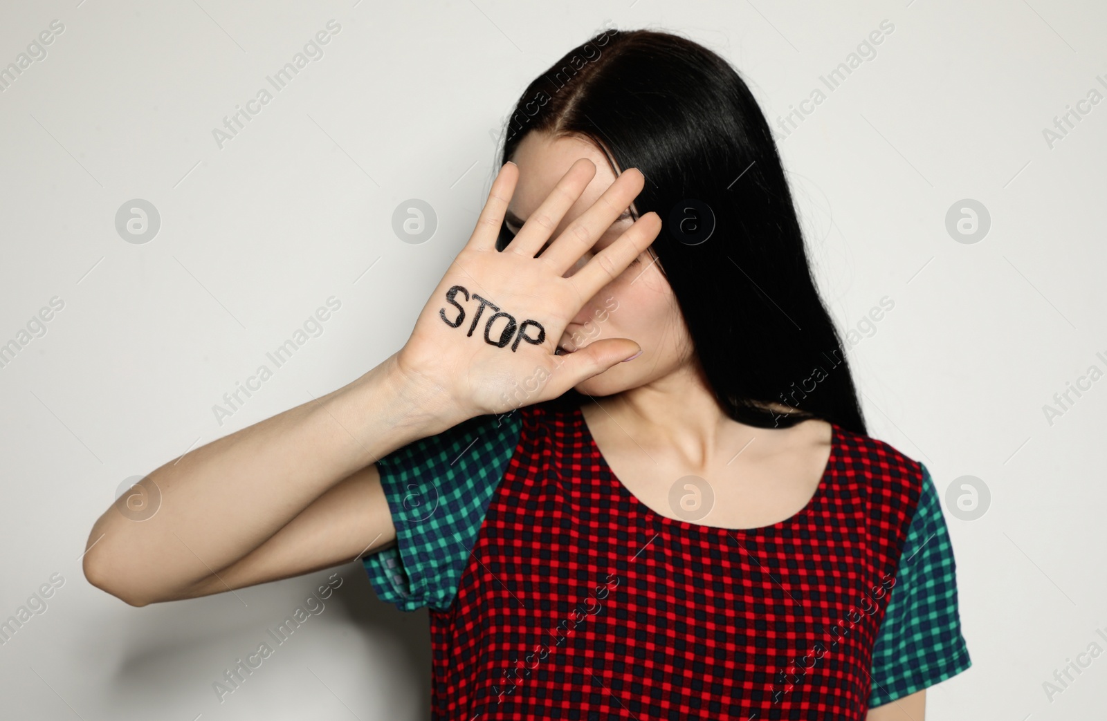 Photo of Young woman with word STOP written on her palm against light background