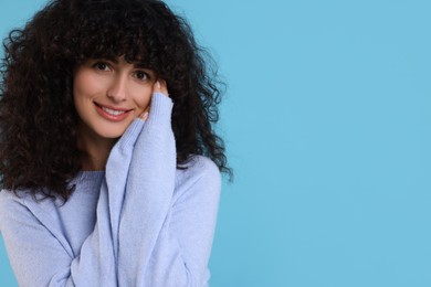 Happy young woman in stylish warm sweater on light blue background, space for text