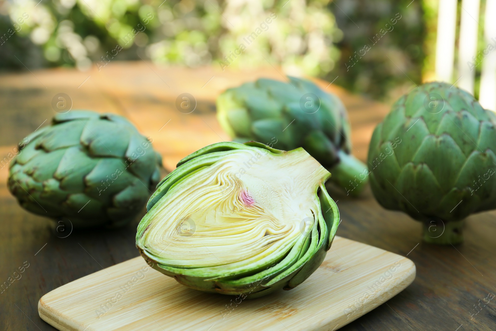Photo of Whole and cut fresh raw artichokes on wooden table outdoors, closeup