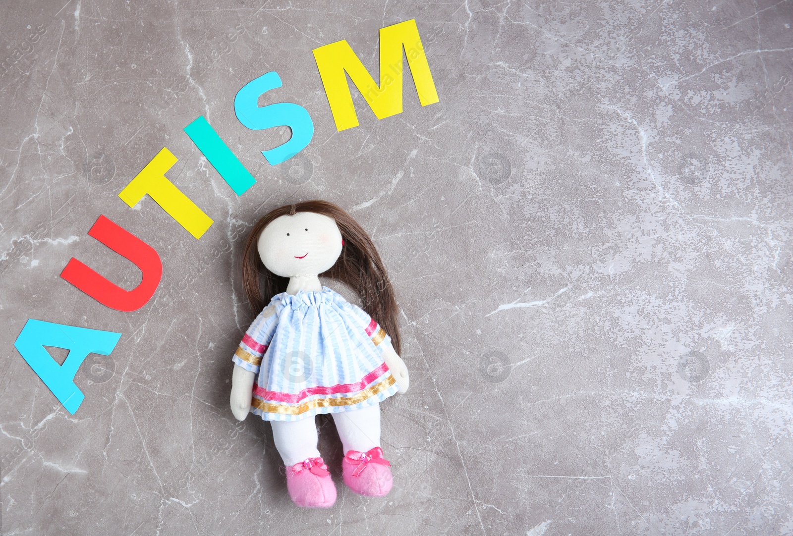 Photo of Word AUTISM and doll on grey background, top view