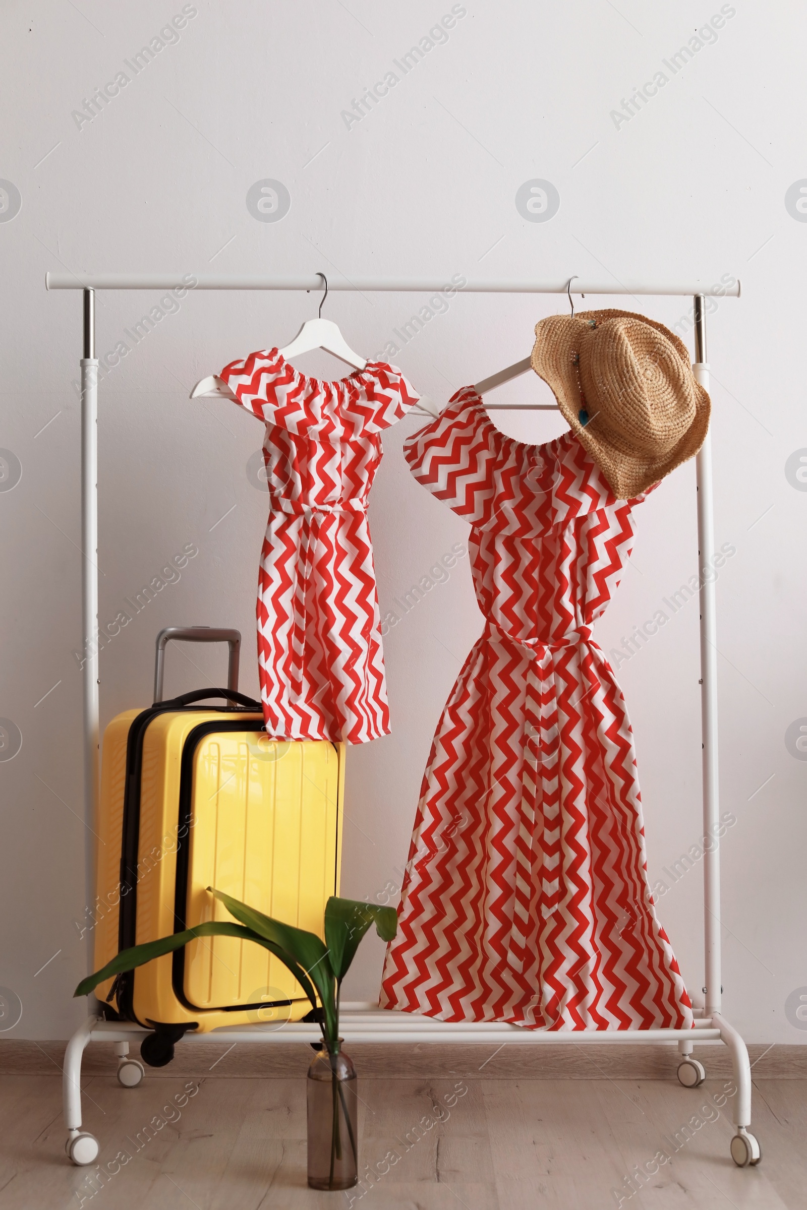 Photo of Packed yellow suitcase and rack with clothes indoors