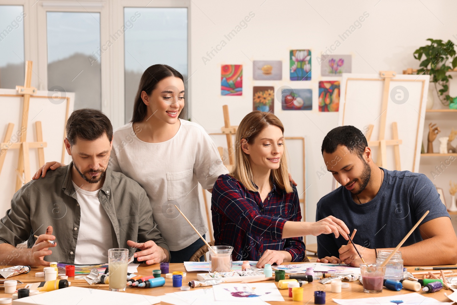 Photo of Artist teaching her students to paint at table in studio. Creative hobby