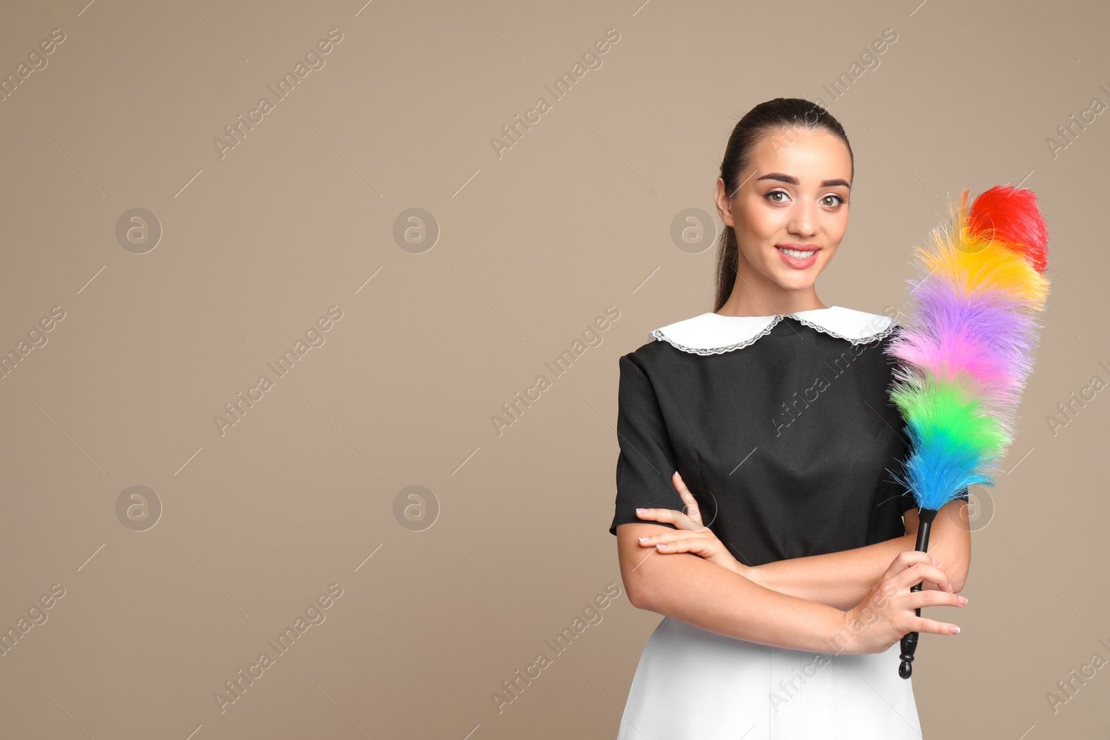 Photo of Young chambermaid with dusting brush on color background