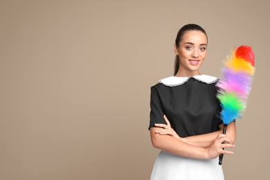 Young chambermaid with dusting brush on color background