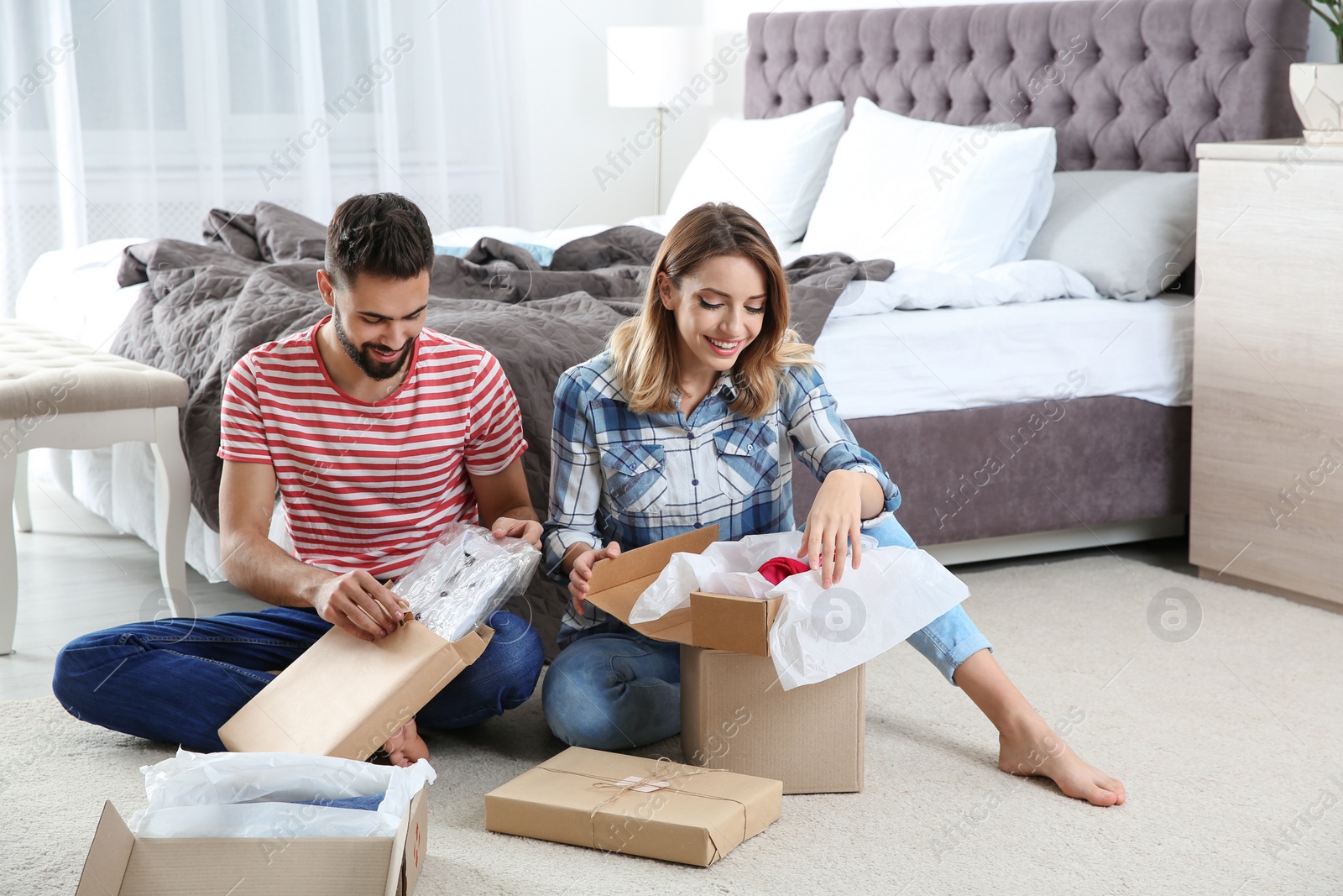 Photo of Young couple opening parcels in bedroom at home