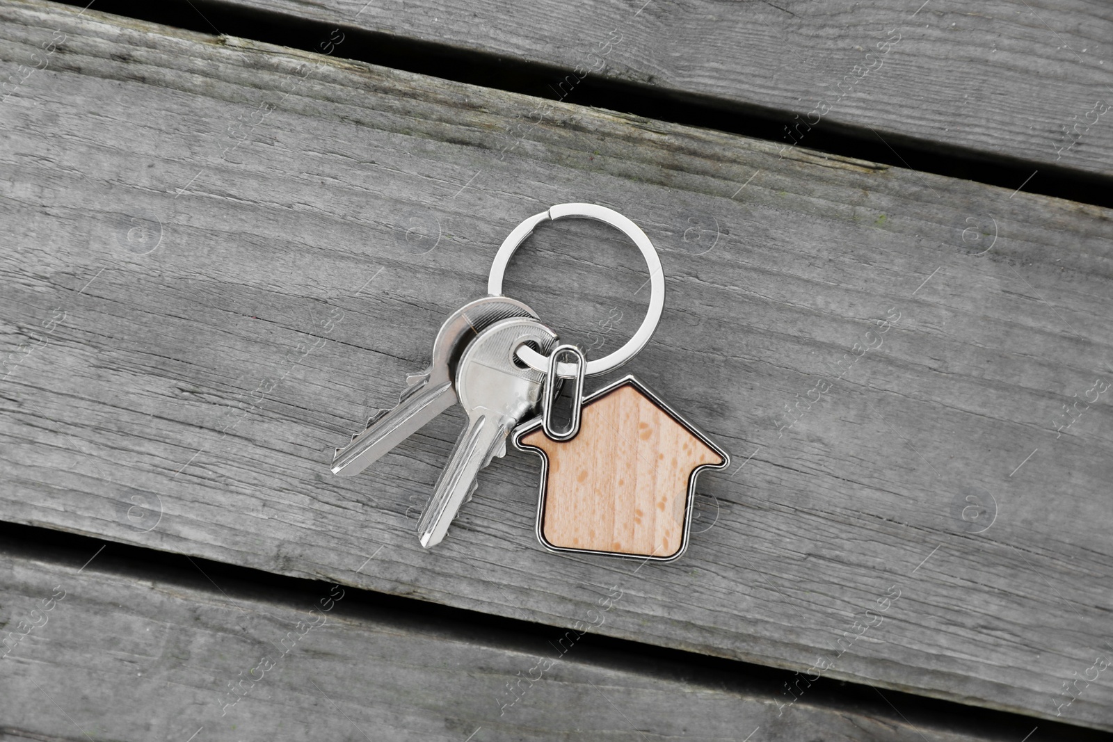 Photo of Keys with trinket in shape of house on wooden table, top view. Real estate agent services