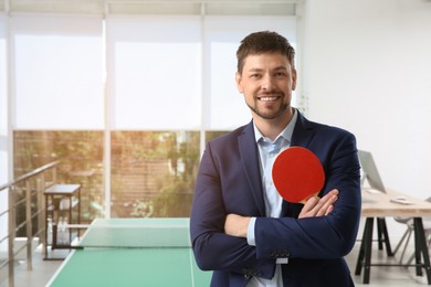 Businessman with tennis racket near ping pong table in office. Space for text