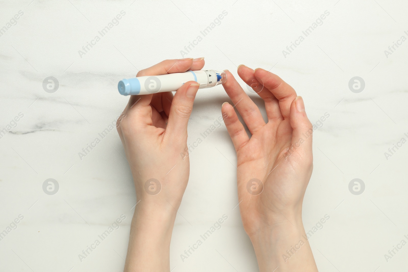 Photo of Diabetes. glucose testing. Woman using lancet pen at white marble table, top view