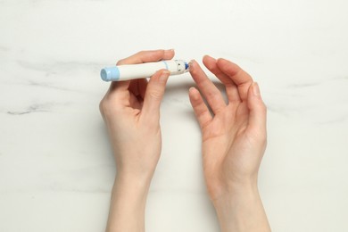 Diabetes. glucose testing. Woman using lancet pen at white marble table, top view