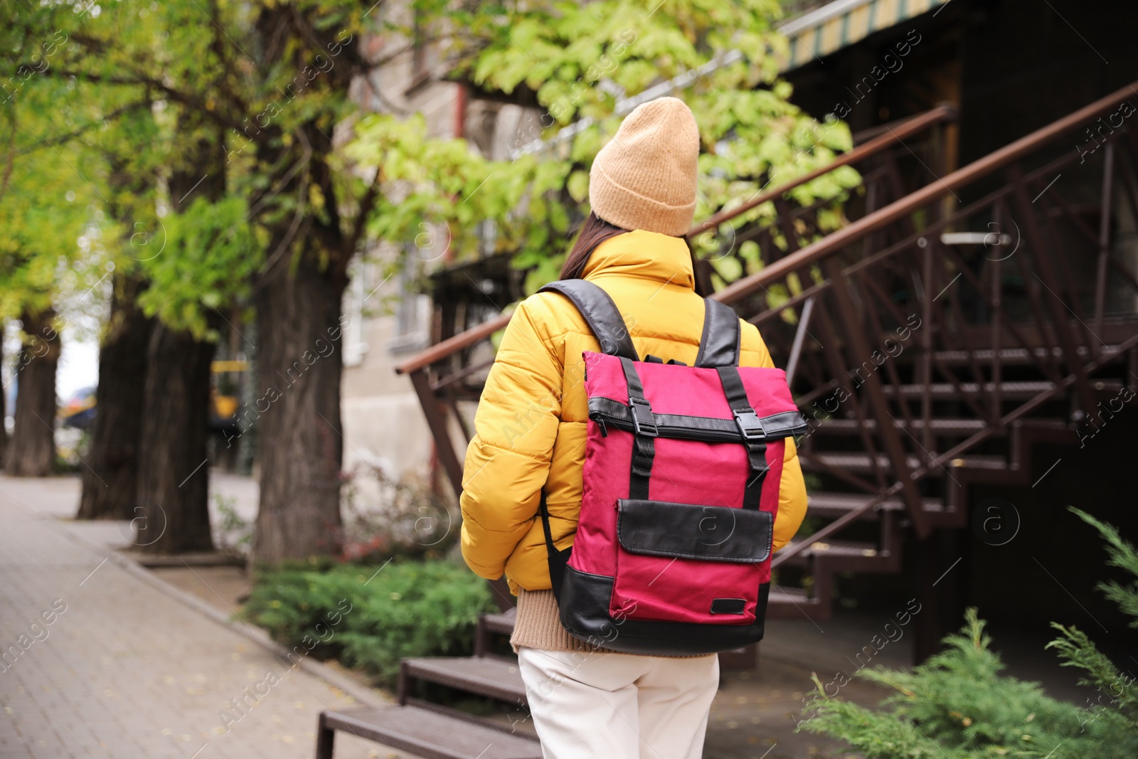 Photo of Female tourist with travel backpack on city street, back view. Urban trip