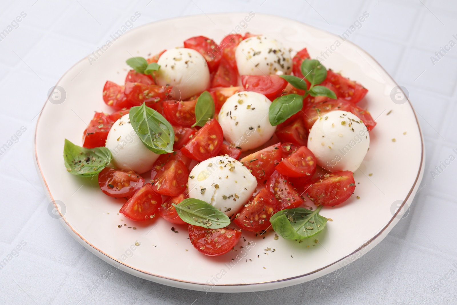 Photo of Tasty salad Caprese with tomatoes, mozzarella balls and basil on white tiled table, closeup