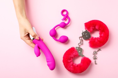Photo of Young woman holding vibrator near sex toys on pink background, top view