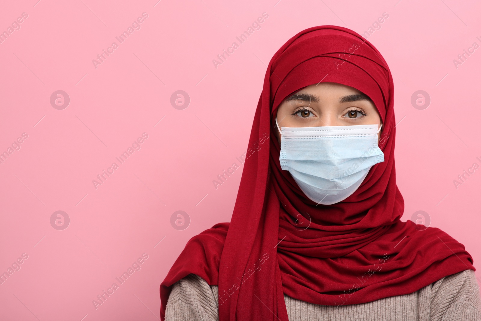 Photo of Muslim woman in hijab and medical mask on pink background, space for text