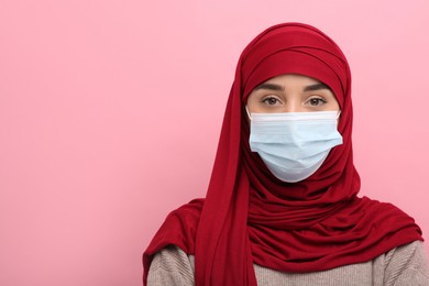 Muslim woman in hijab and medical mask on pink background, space for text