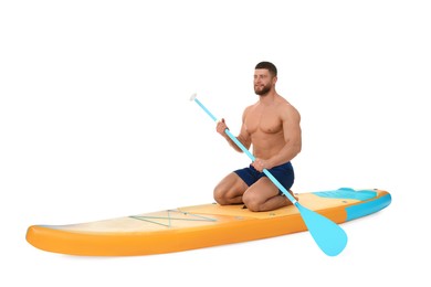Handsome man with paddle on orange SUP board against white background