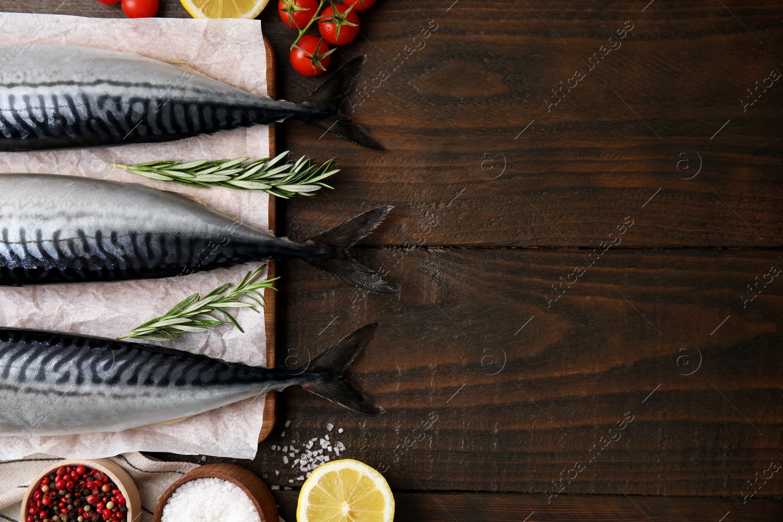 Photo of Raw mackerel, tomatoes and rosemary on wooden table, flat lay. Space for text