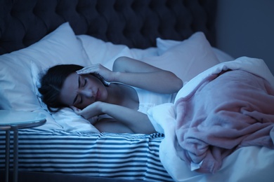 Photo of Young woman suffering from headache while lying in bed at night. Sleeping problems