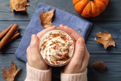 Photo of Woman holding tasty pumpkin latte at blue wooden table, top view