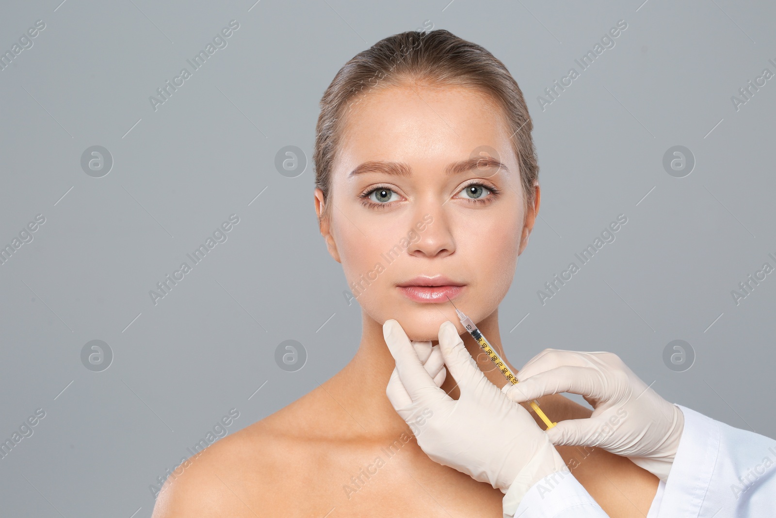 Photo of Young woman getting lips injection on grey background. Cosmetic surgery