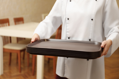 Photo of School canteen worker holding plastic trays for food indoors, closeup