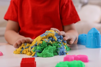 Little boy playing with bright kinetic sand at table indoors, closeup