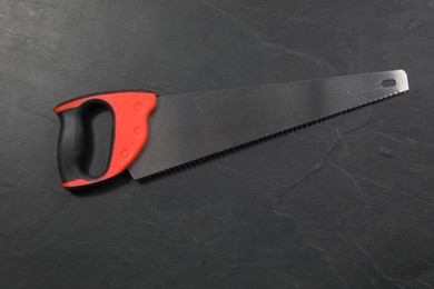 Photo of Saw with colorful handle on black textured background, top view