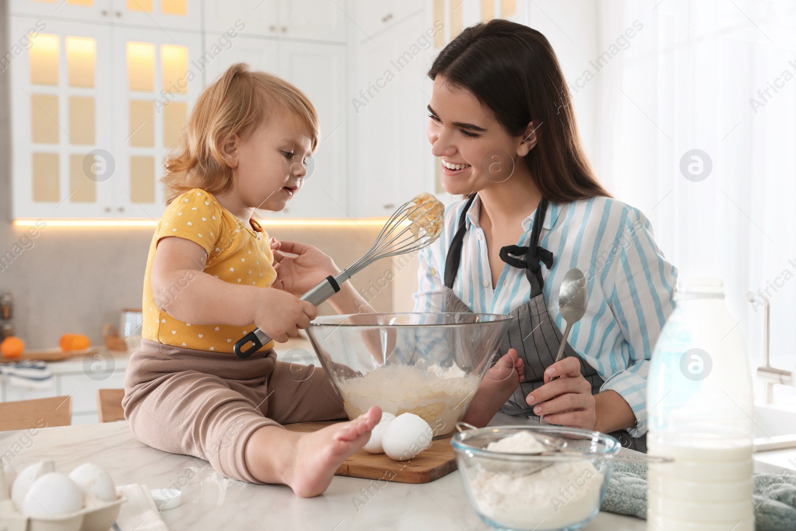 Photo of Mother and her little daughter cooking dough together in kitchen