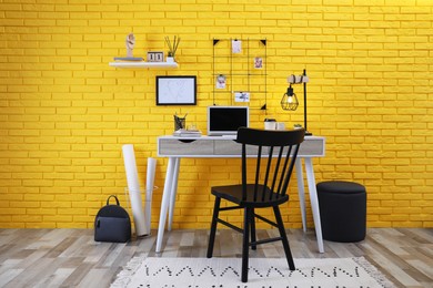 Photo of Stylish home office interior with comfortable workplace near yellow brick wall