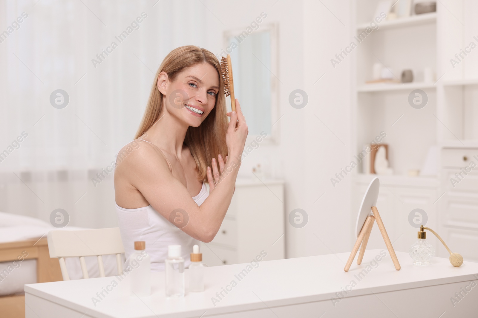 Photo of Beautiful woman brushing her hair at vanity in bedroom