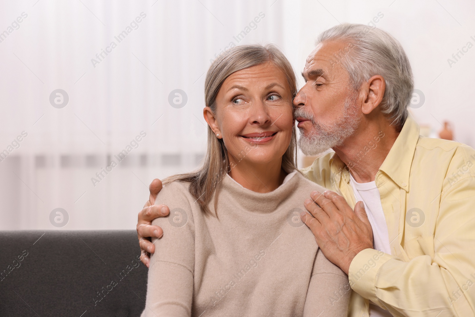 Photo of Senior man kissing his beloved woman at home, space for text