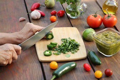 Photo of Woman cutting pepper for tasty salsa sauce at wooden table