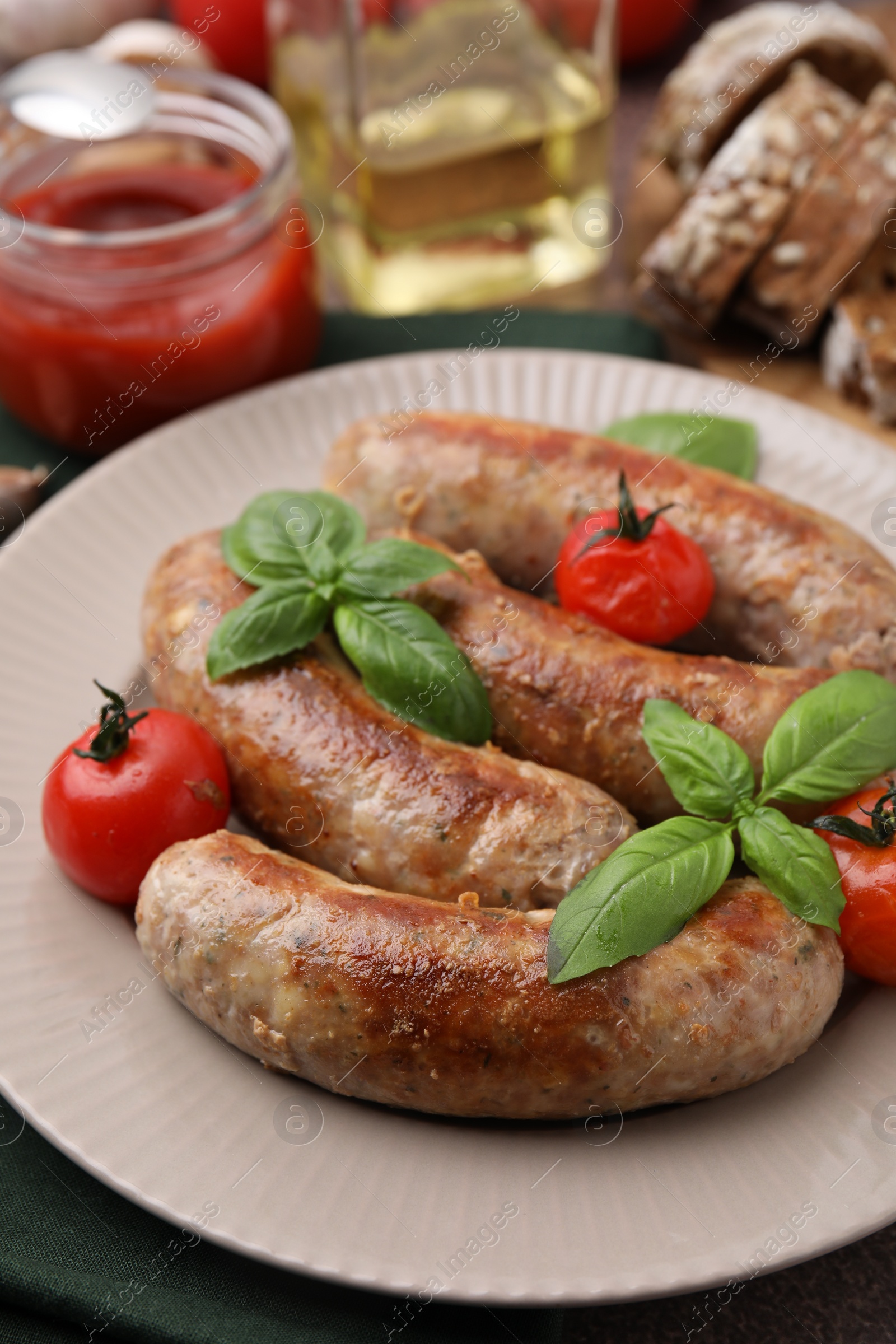 Photo of Plate with tasty homemade sausages, basil leaves and tomatoes on table, closeup