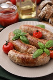 Plate with tasty homemade sausages, basil leaves and tomatoes on table, closeup