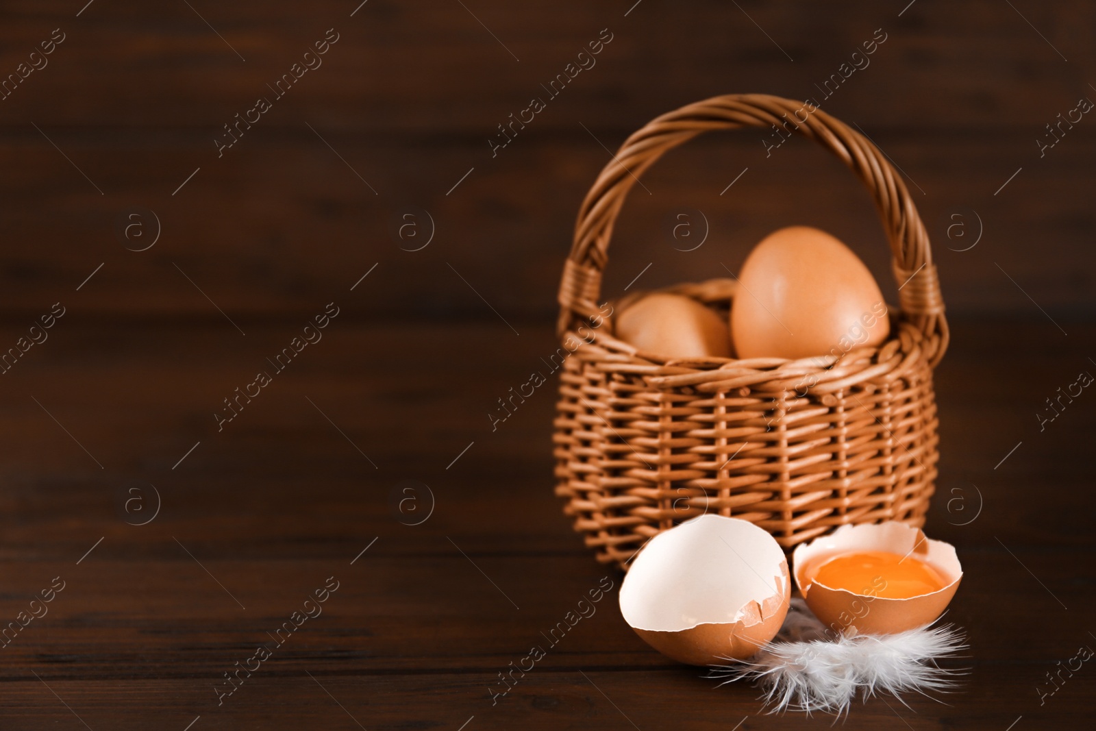 Photo of Raw chicken eggs and feather on wooden table. Space for text