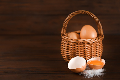 Raw chicken eggs and feather on wooden table. Space for text