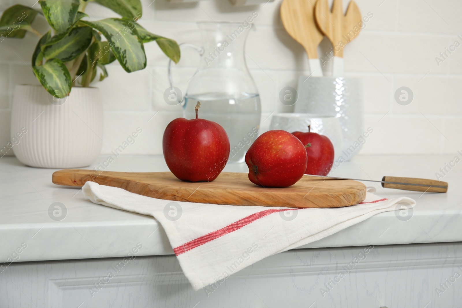 Photo of Clean towel and wooden board with ripe apples on countertop in kitchen